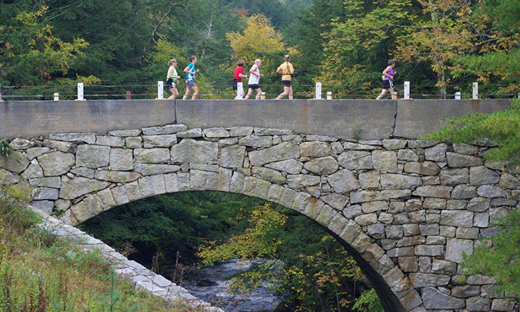 Runners cross a pedestrian stone bridge at the Clarence DeMar Marathon
